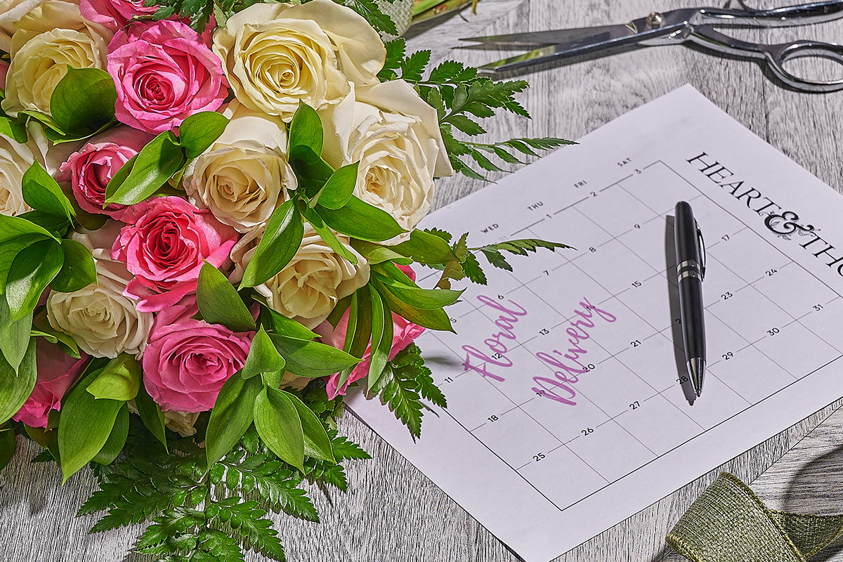 Bouquet of pink and white roses with a calendar and pen on a wooden surface