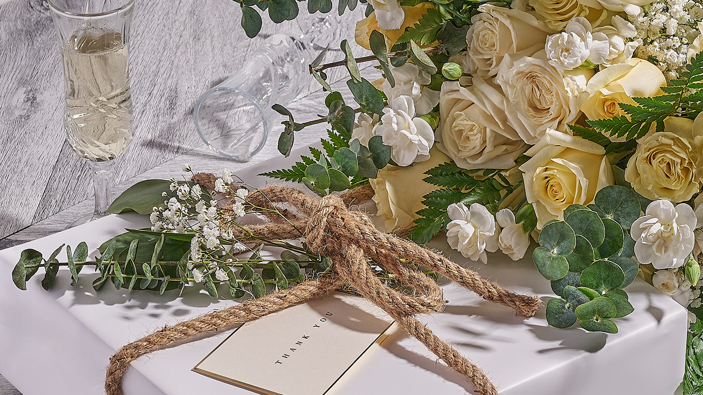 Floral arrangement with white and yellow flowers tied with twine on a wooden surface.