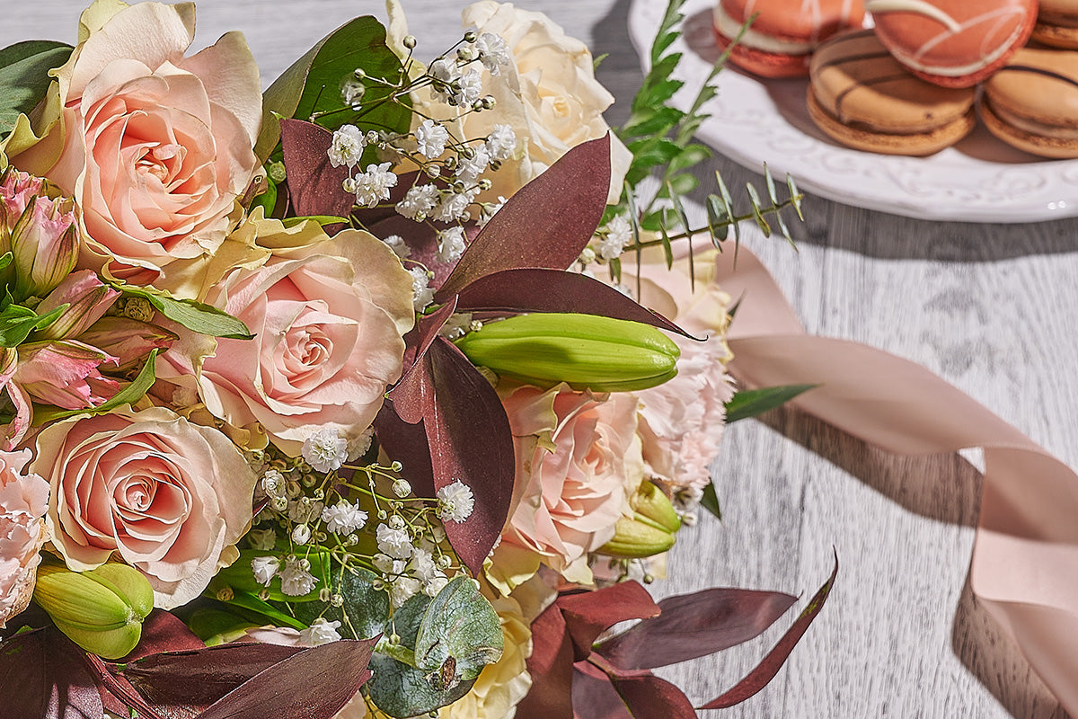 Bouquet of pink and yellow roses with greenery on a wooden table.